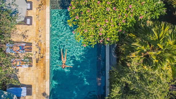 A swimming pool with clear water, surrounded by lush greenery and a tiled deck area with lounge chairs. - Minabali Bunga'lo (Tulamben)
