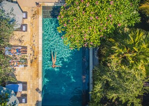 A swimming pool with clear water, surrounded by lush greenery and a tiled deck area with lounge chairs. - Minabali Bunga'lo (Tulamben)