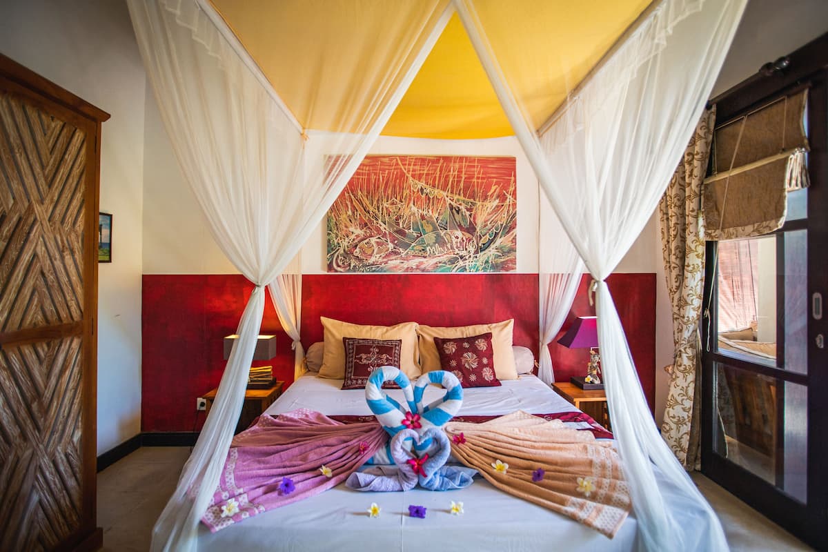 A room with a bed under a canopy, a red wall, and a painting above the bed.