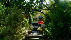 A garden pathway leading to a building with a red umbrella. - Minabali Bunga'lo (Tulamben)