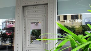 Una entrada de hotel moderna con una puerta metálica decorativa y un ventanal que refleja los alrededores.