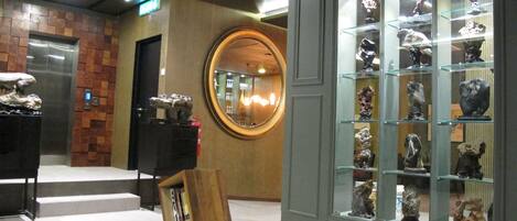 A lobby with a reception desk, a mirror, and a display of sculptures.