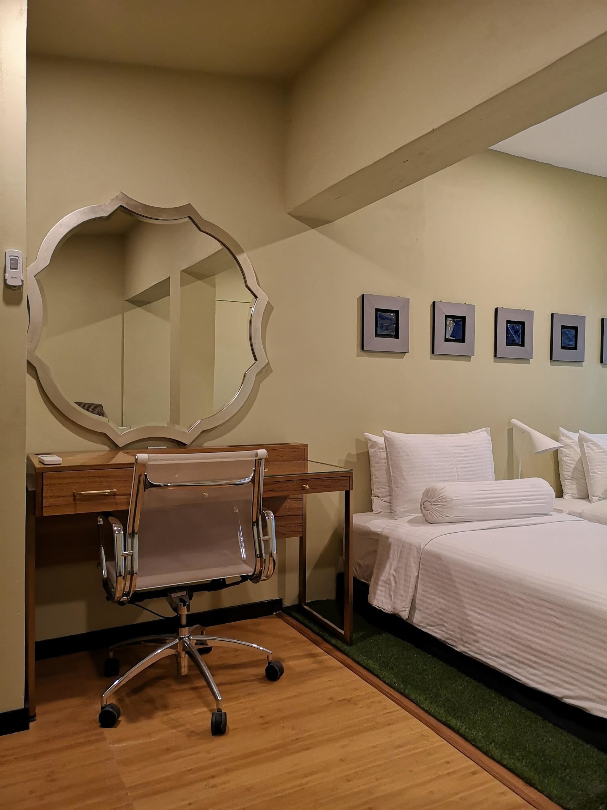 Une chambre d’hôtel avec un bureau en bois, un grand miroir, un lit avec une literie blanche et un petit téléviseur fixé au mur.