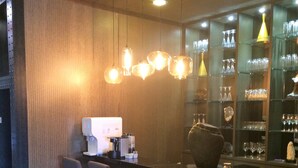 Una zona de bar con mostrador de madera, taburetes y lámparas colgantes.