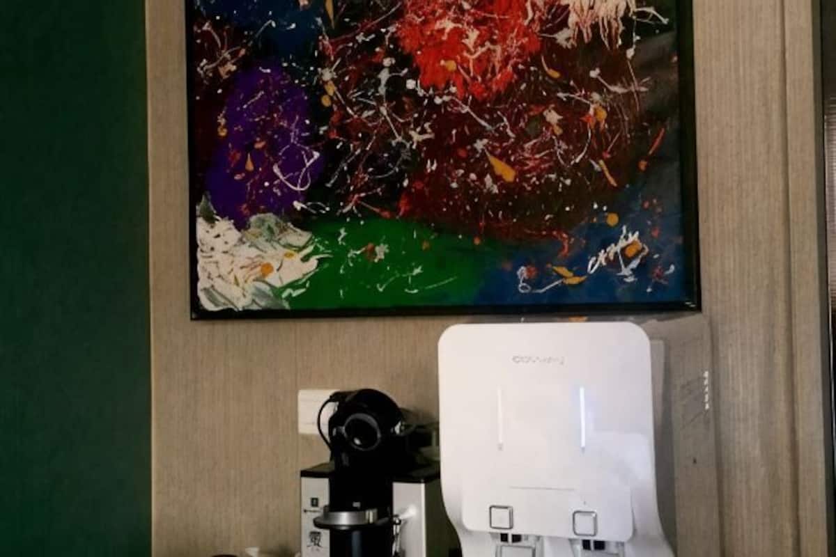 Una habitación con un cuadro abstracto grande en la pared, una cámara sobre un trípode y un dispositivo blanco en el suelo.