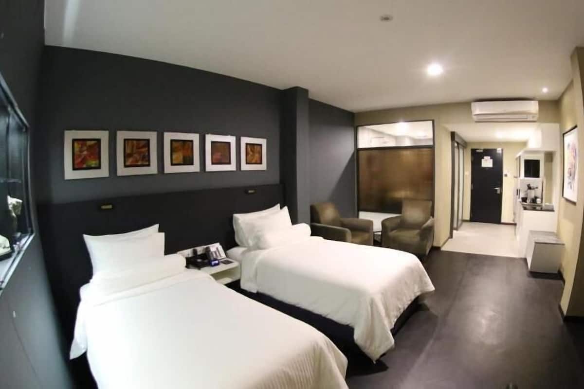 A hotel room with two beds, a desk, a chair, a TV, and an air conditioning unit.