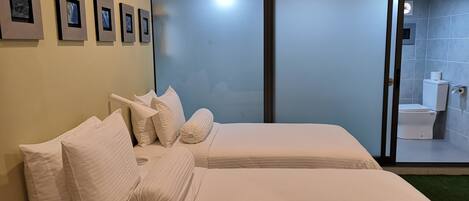 Habitación de hotel con dos camas, un ventanal grande y un baño visible a través de la puerta de vidrio.