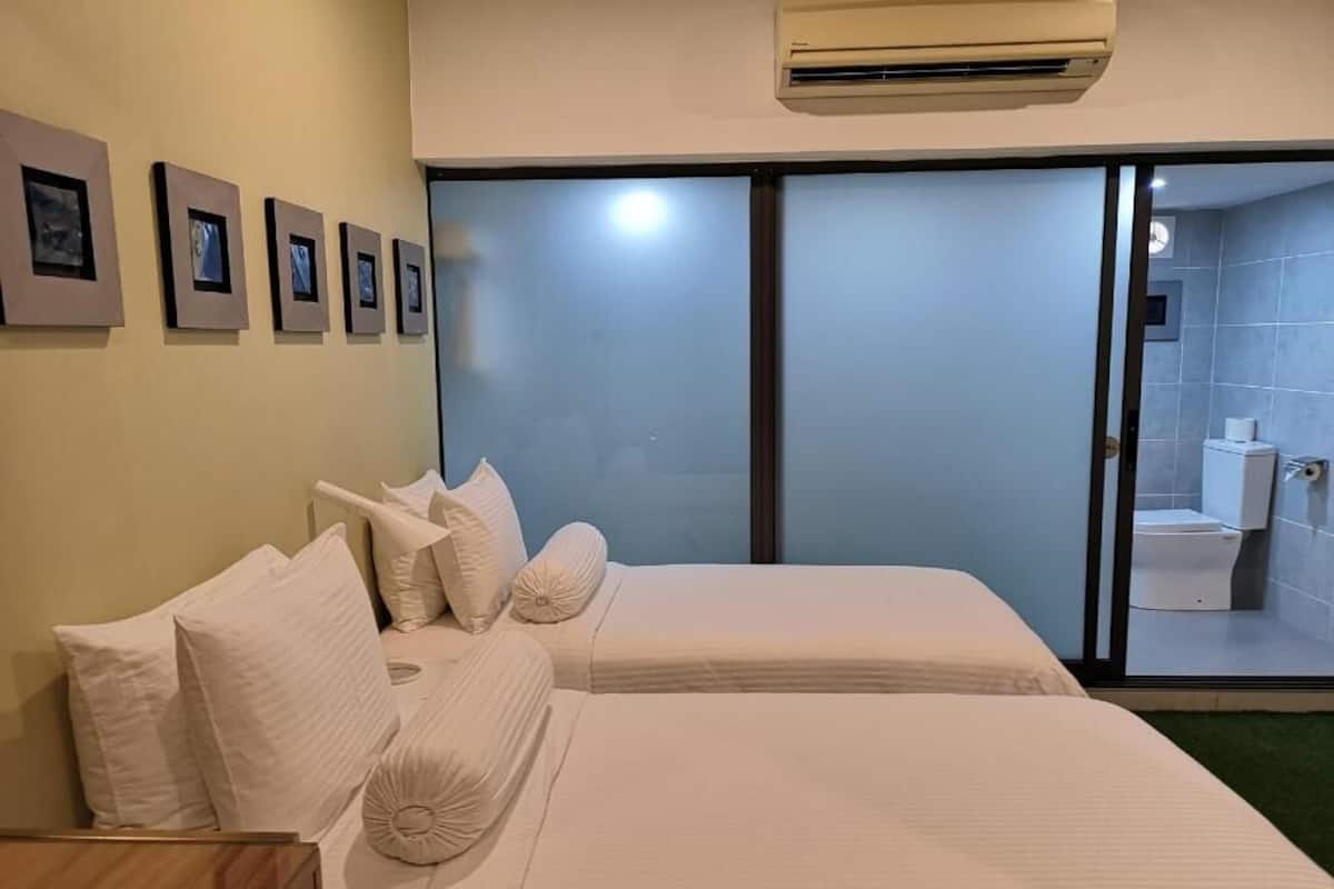A hotel room with two beds, a wooden nightstand, a wall-mounted air conditioner, and a large sliding glass door leading to a bathroom.