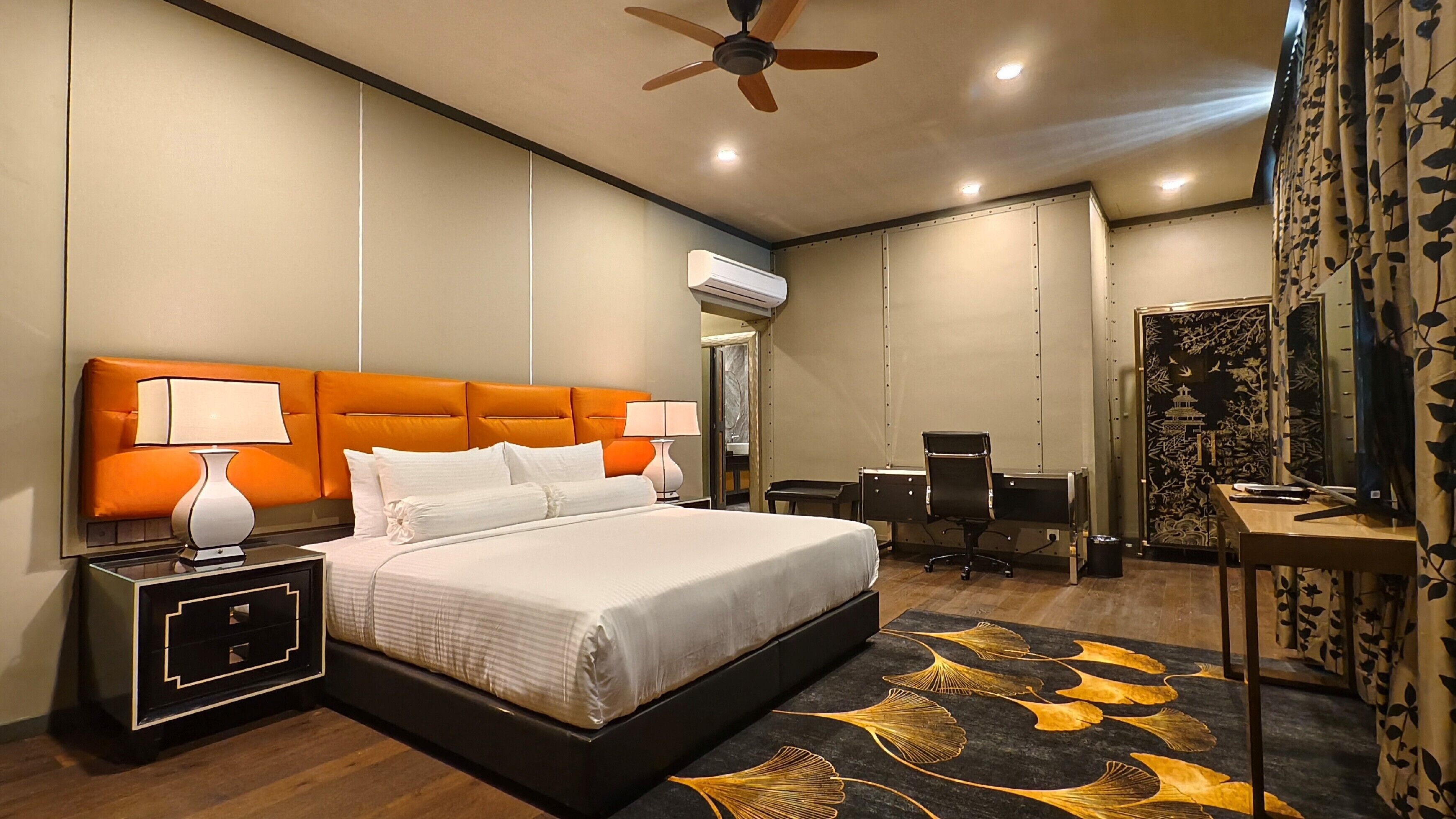A hotel room with a large bed, a desk, a chair, an air conditioning unit, and a ceiling fan.