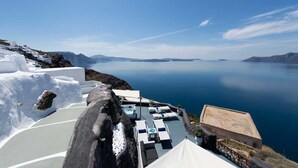 A seaside terrace with white buildings, a pool, and lounge chairs overlooking the sea.