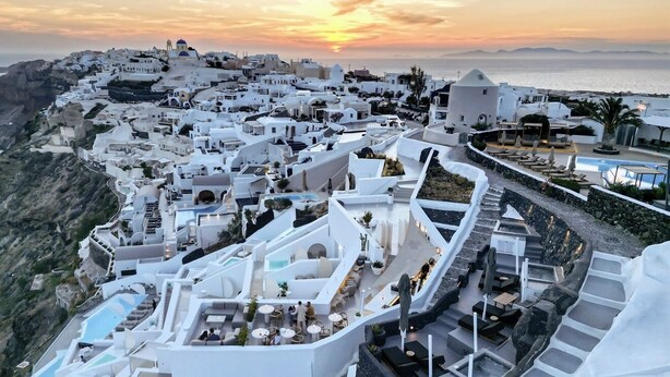 A coastal town with white buildings, outdoor seating areas, and a pool.