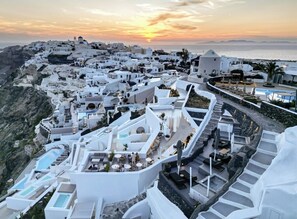 A coastal town with white buildings, outdoor seating areas, and a pool. - Enalion Suites (Santorini)