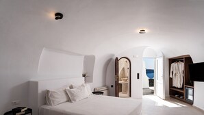 A modern bedroom with a large bed, a bedside table, a wardrobe, and a view of the sea.