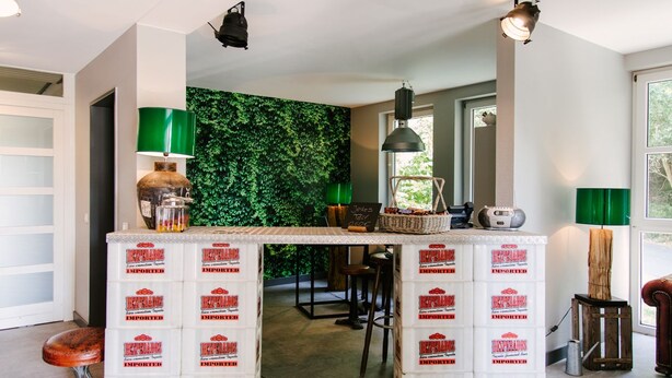 Une cuisine avec un mur recouvert de plantes vertes, un comptoir de bar fait de caisses blanches et un luminaire suspendu.