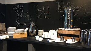 Un coin café avec un tableau noir affichant les plats et les prix du menu, une machine à café, ainsi que diverses tasses et assiettes.