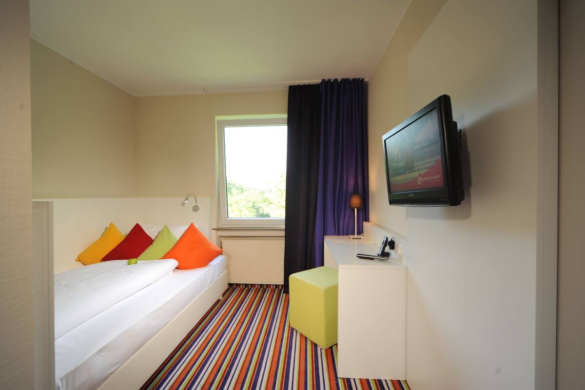 A hotel room with a bed, a desk, a television, and a window with curtains.