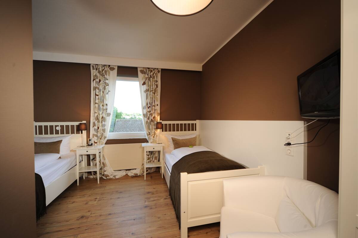 A bedroom with two single beds, a desk, a chair, and a TV mounted on the wall.