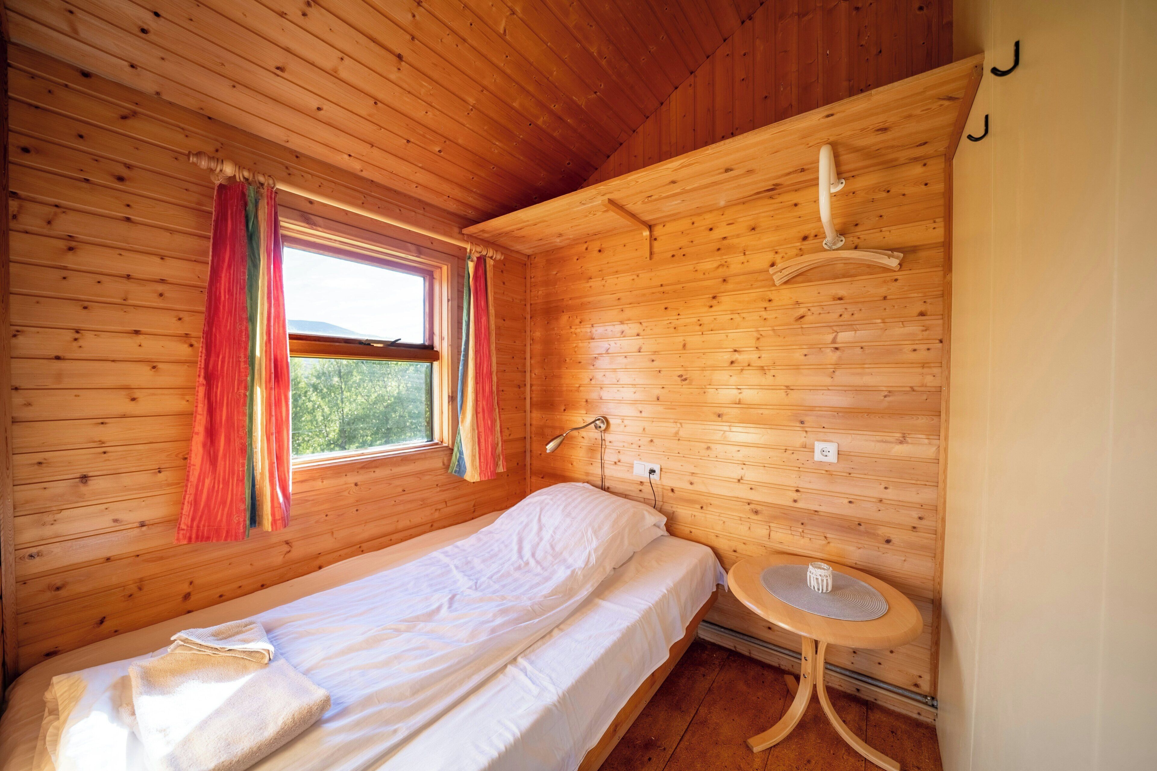 A wooden room with a bed, a small table, and a window with curtains.