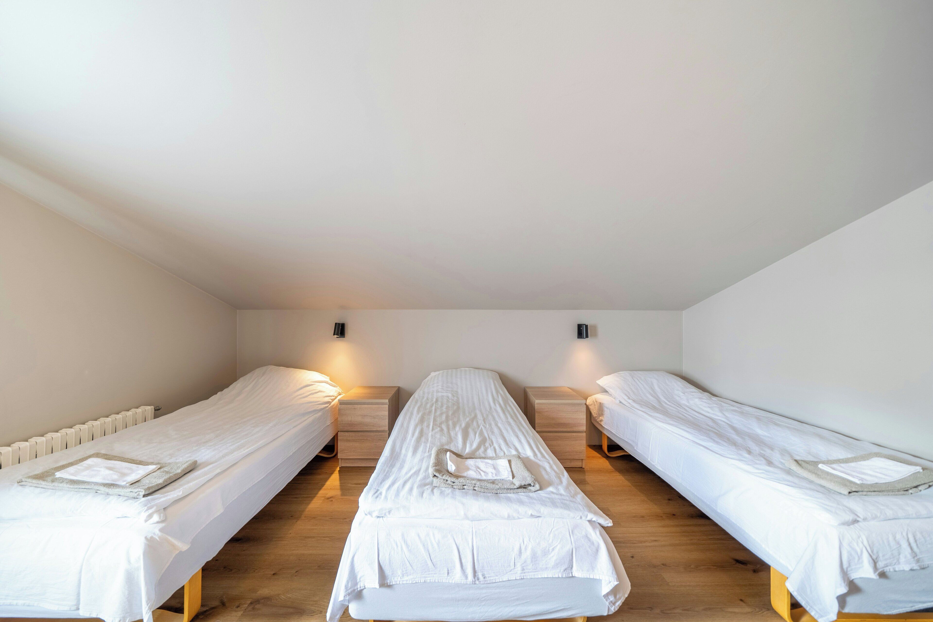 A room with three single beds, wooden flooring, and white walls.