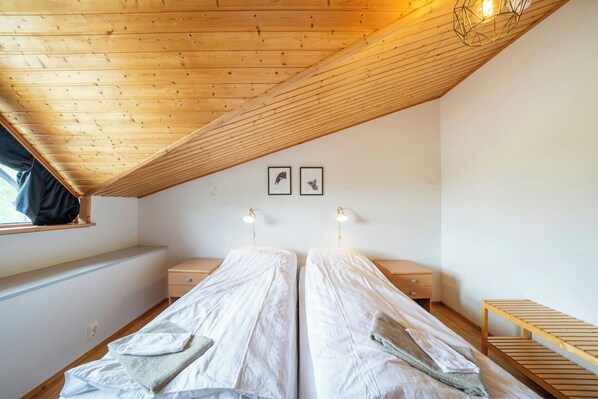 Un dormitorio con dos camas, vigas de madera en el techo, una ventana y luces fijadas a la pared.