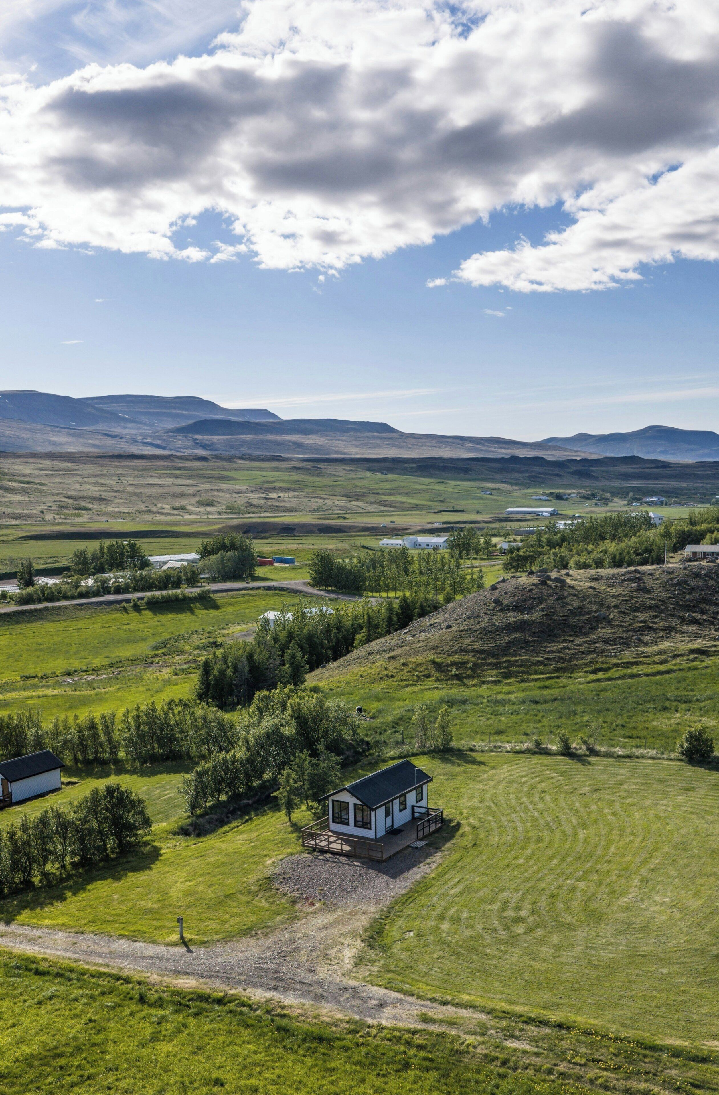 A rural landscape with a house on a hill, surrounded by green fields and distant mountains.