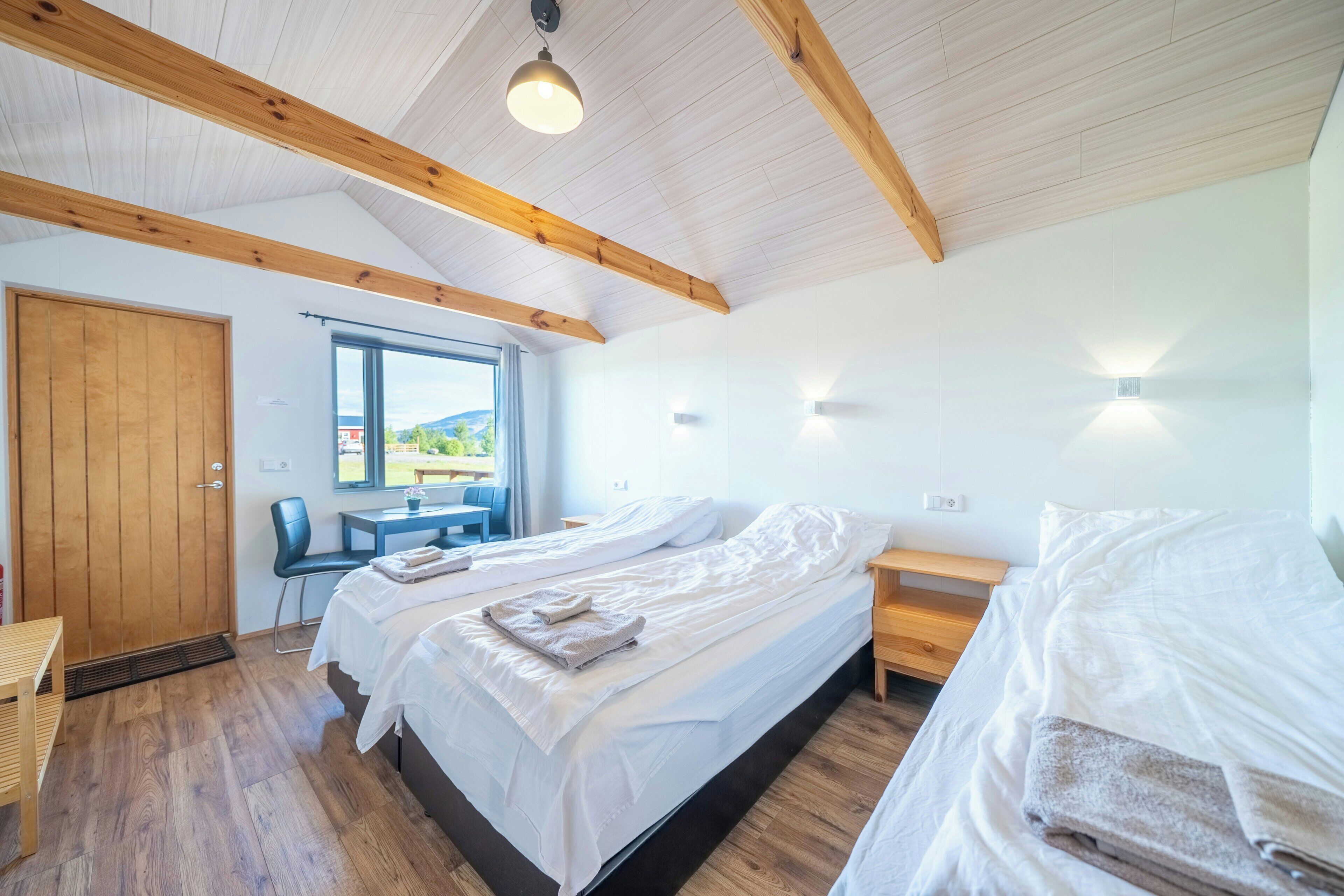 Une chambre avec deux lits, des poutres en bois, une fenêtre et un bureau.