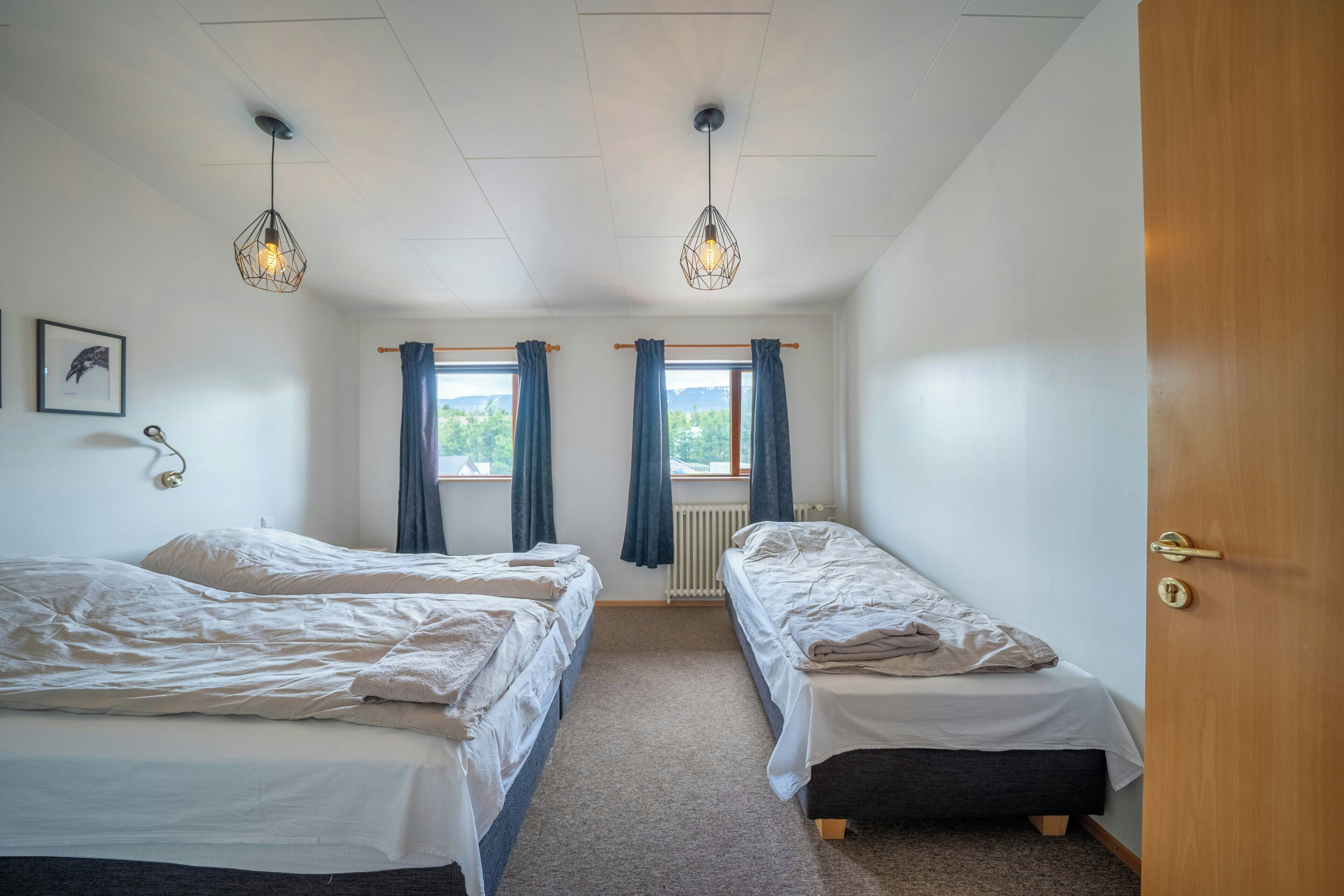 Una habitación con dos camas, una puerta de madera y una ventana con cortinas.