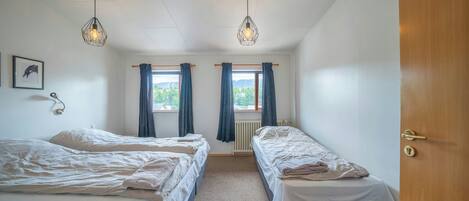 Una habitación con dos camas, una puerta de madera y una ventana con cortinas.