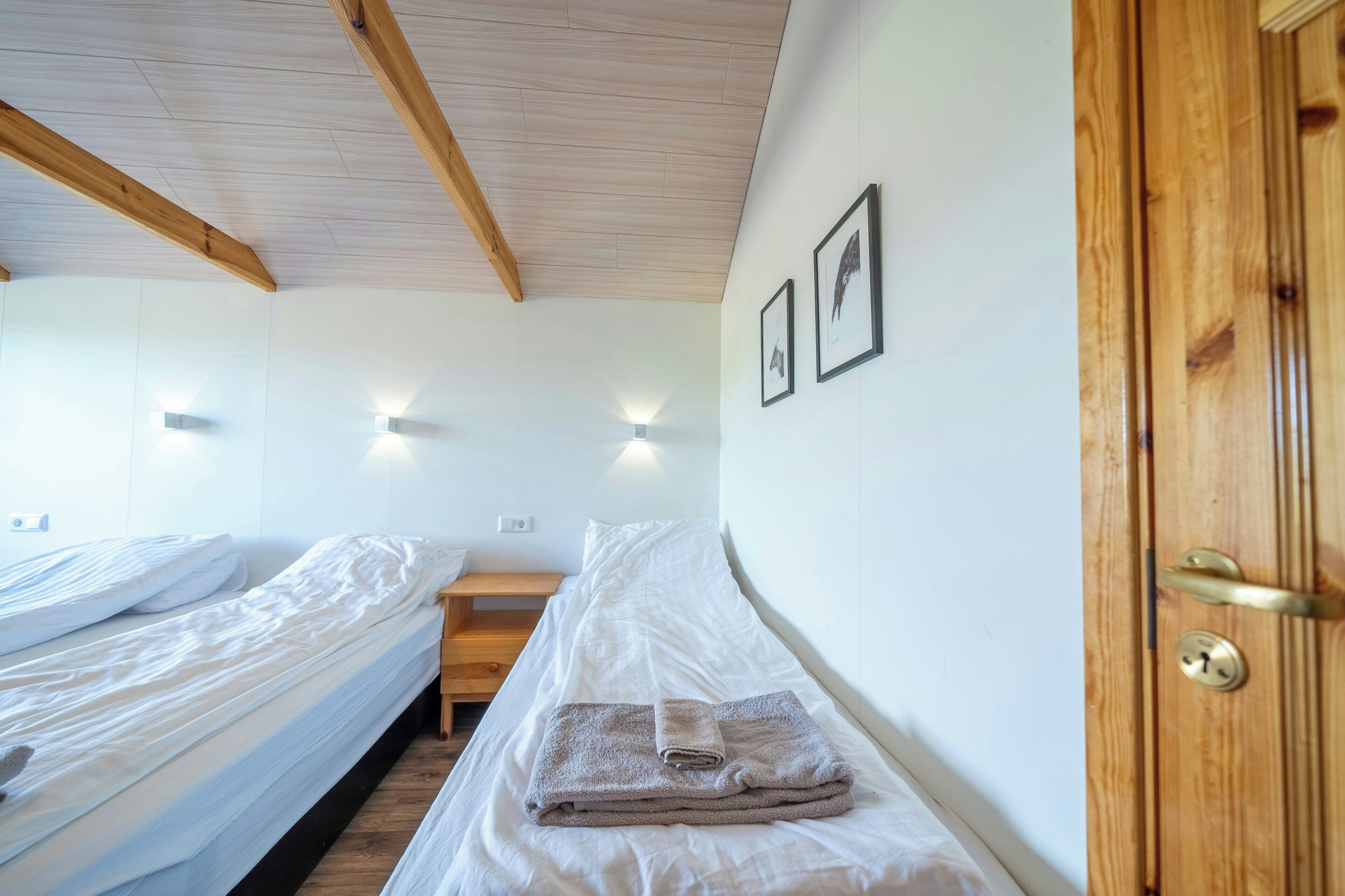 A room with two beds, a wooden door, and wall-mounted lights.