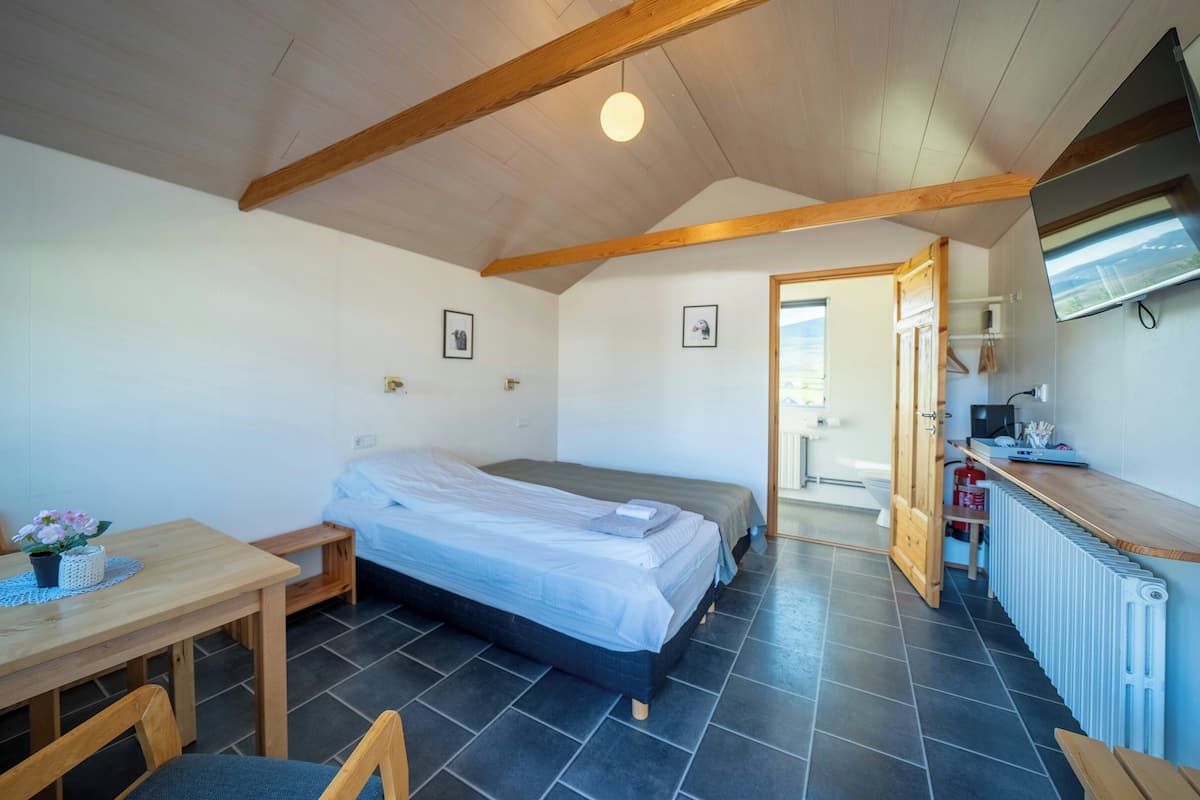 A bedroom with a bed, a desk, a chair, a radiator, and a door leading to another room.