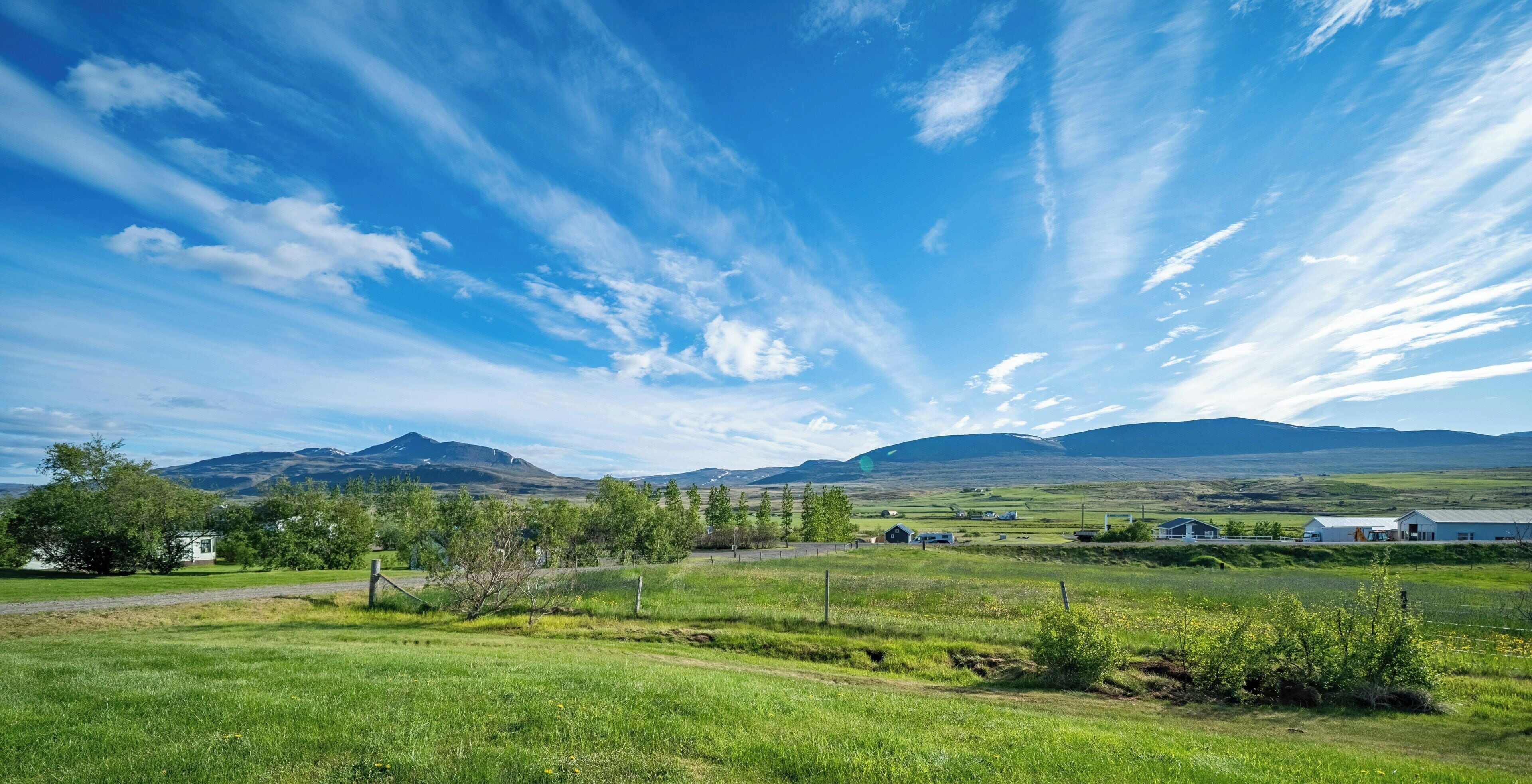Paisaje rural con cielo despejado, campos verdes y montañas lejanas.