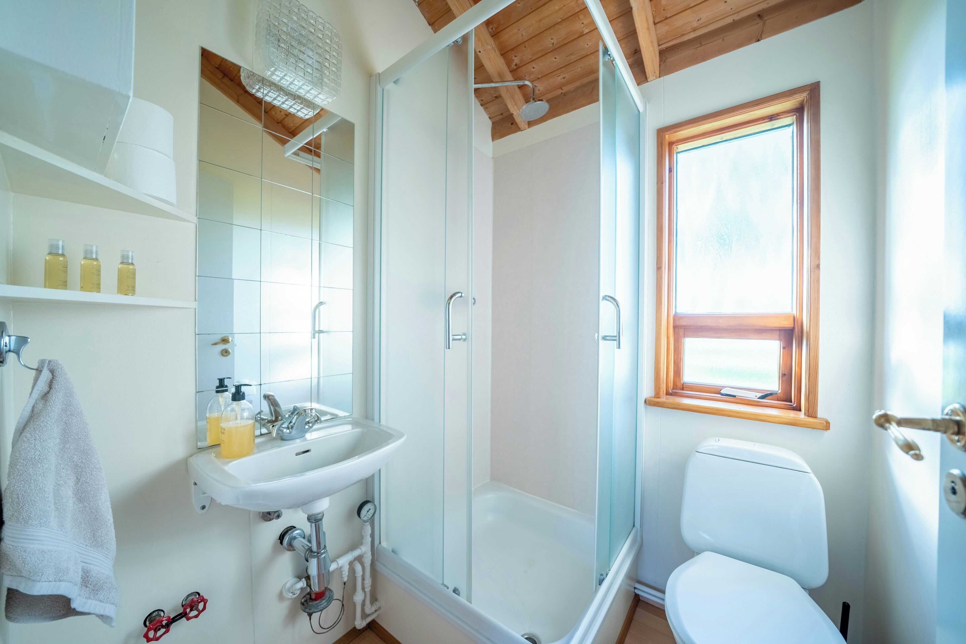 A bathroom with a glass-enclosed shower, a white sink, a toilet, and a window.