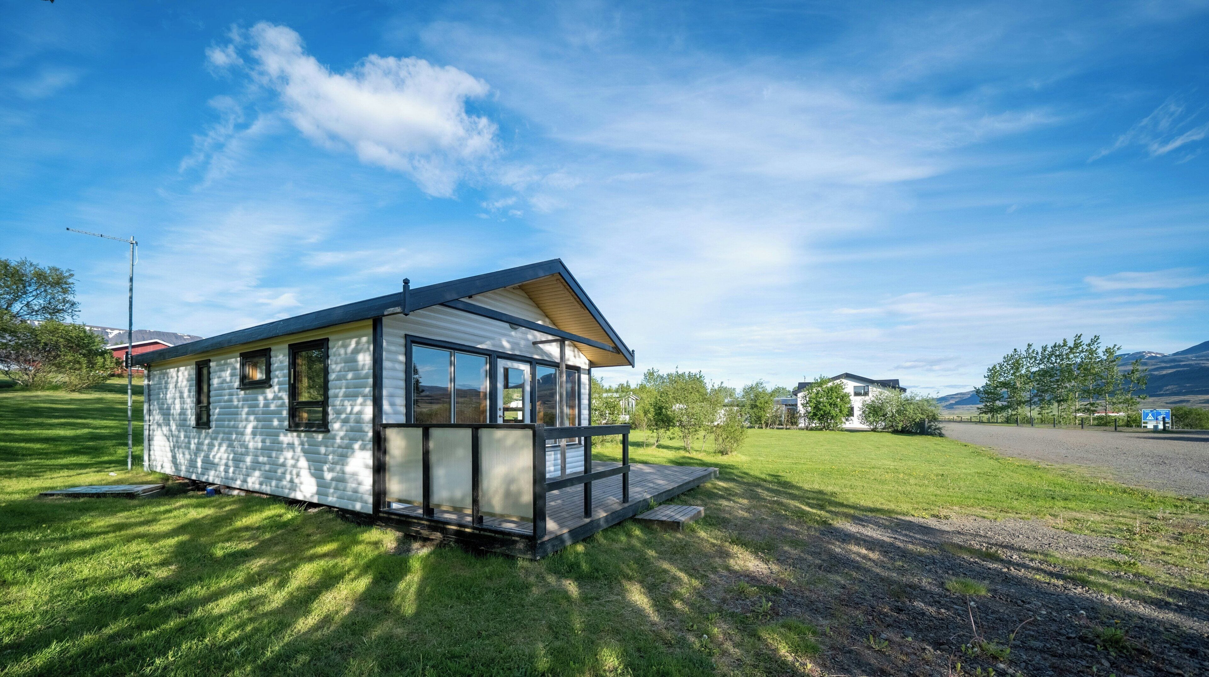 A small, single-story house with a porch, surrounded by a grassy area and a clear sky.