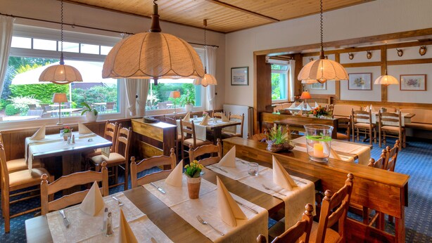 Un restaurant avec des tables et des chaises en bois, des lampes suspendues et des œuvres d’art encadrées accrochées aux murs.