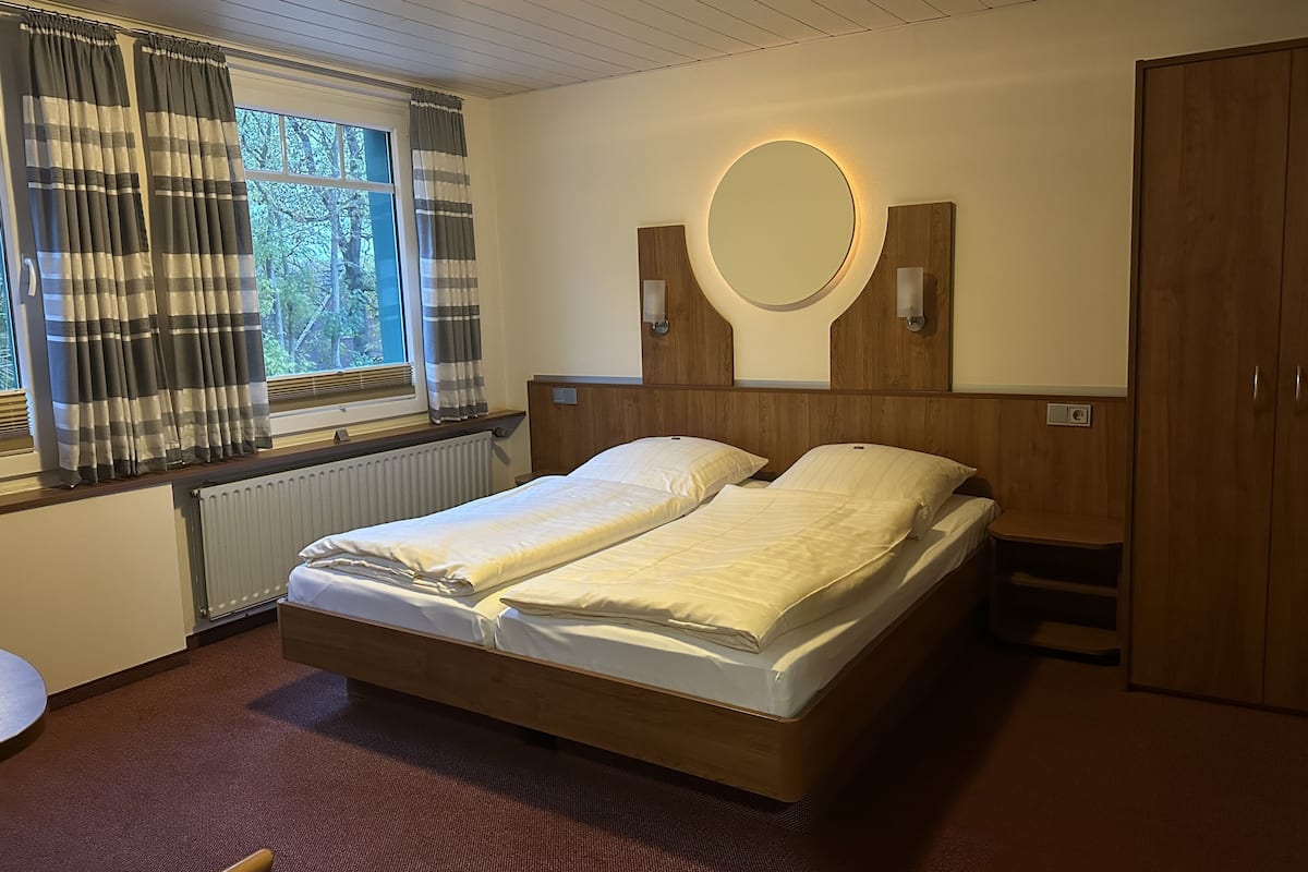 A double bed with a wooden headboard, a round mirror, and a radiator.