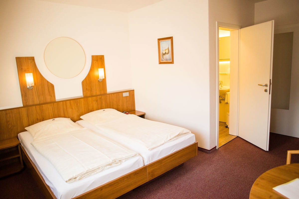 A double bed with a wooden headboard, two bedside tables, a round mirror, and a small framed picture on the wall.