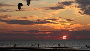 Un coucher de soleil sur l’océan, avec les silhouettes de personnes et de cerfs-volants.