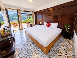 A hotel room with a large bed, a desk with a chair, a small table with a vase, and a view of the outdoors. - Sapa Village Hotel Sky Lounge & Spa (Sa Pa)