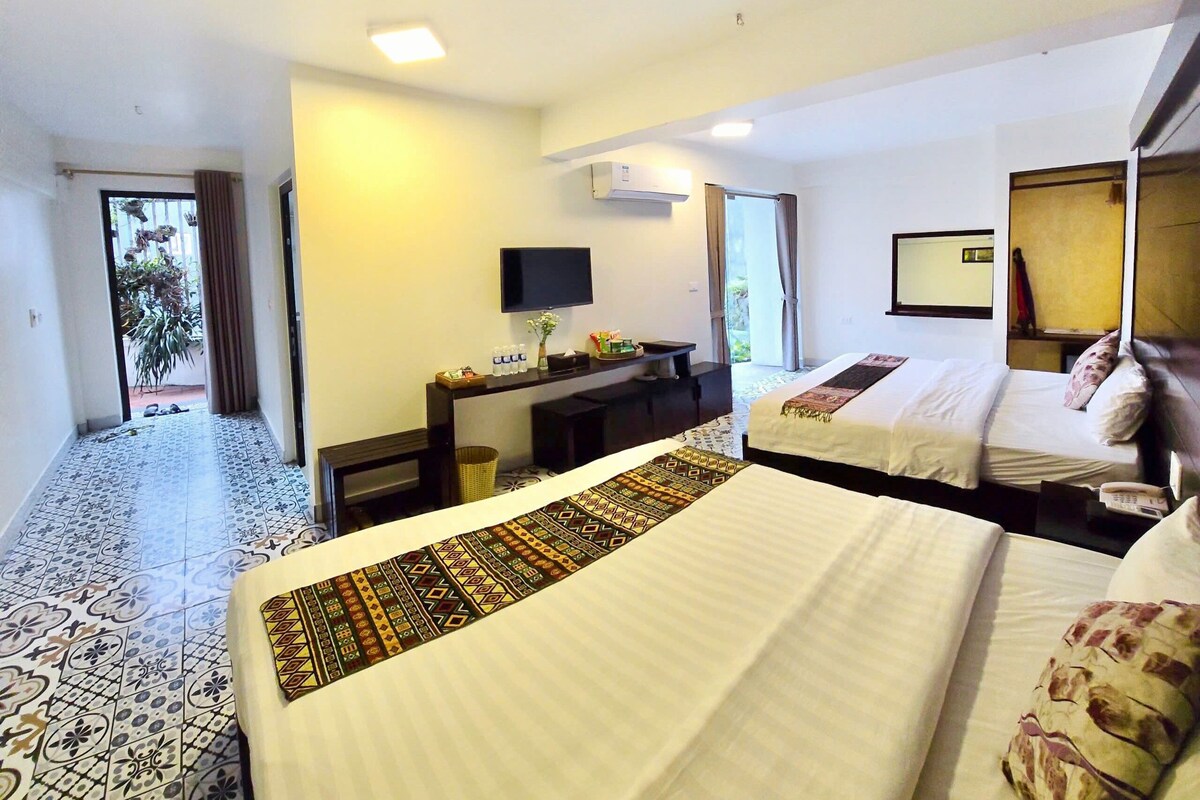 A hotel room with two beds, a desk with a flat-screen TV, and a bathroom visible through an open door.