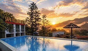 A hotel with a swimming pool, a sign reading 'SAPA VILLAGE HOTEL,' and a sunset in the background. - Sapa Village Hotel Sky Lounge & Spa (Sa Pa)