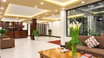A hotel reception area with a reception desk, a receptionist, and a seating area with a sofa and a coffee table.
