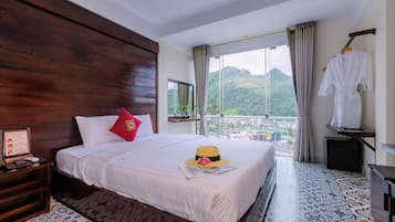 Una habitación de hotel con una cama grande, cabecero de madera, vistas a las montañas y un balcón con una bata blanca colgada.