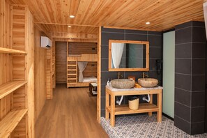 Ambiente interno in legno con bagno dotato di due lavabi in pietra, uno specchio e un mobile bagno in legno.