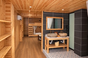 A wooden interior with a bathroom featuring two stone sinks, a mirror, and a wooden vanity.