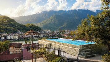 A swimming pool with a stone border, surrounded by a stone staircase and a metal railing, overlooking a town and mountains.
