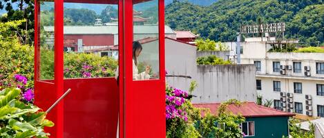 A red cable car with a person inside, surrounded by lush greenery and mountains in the background.