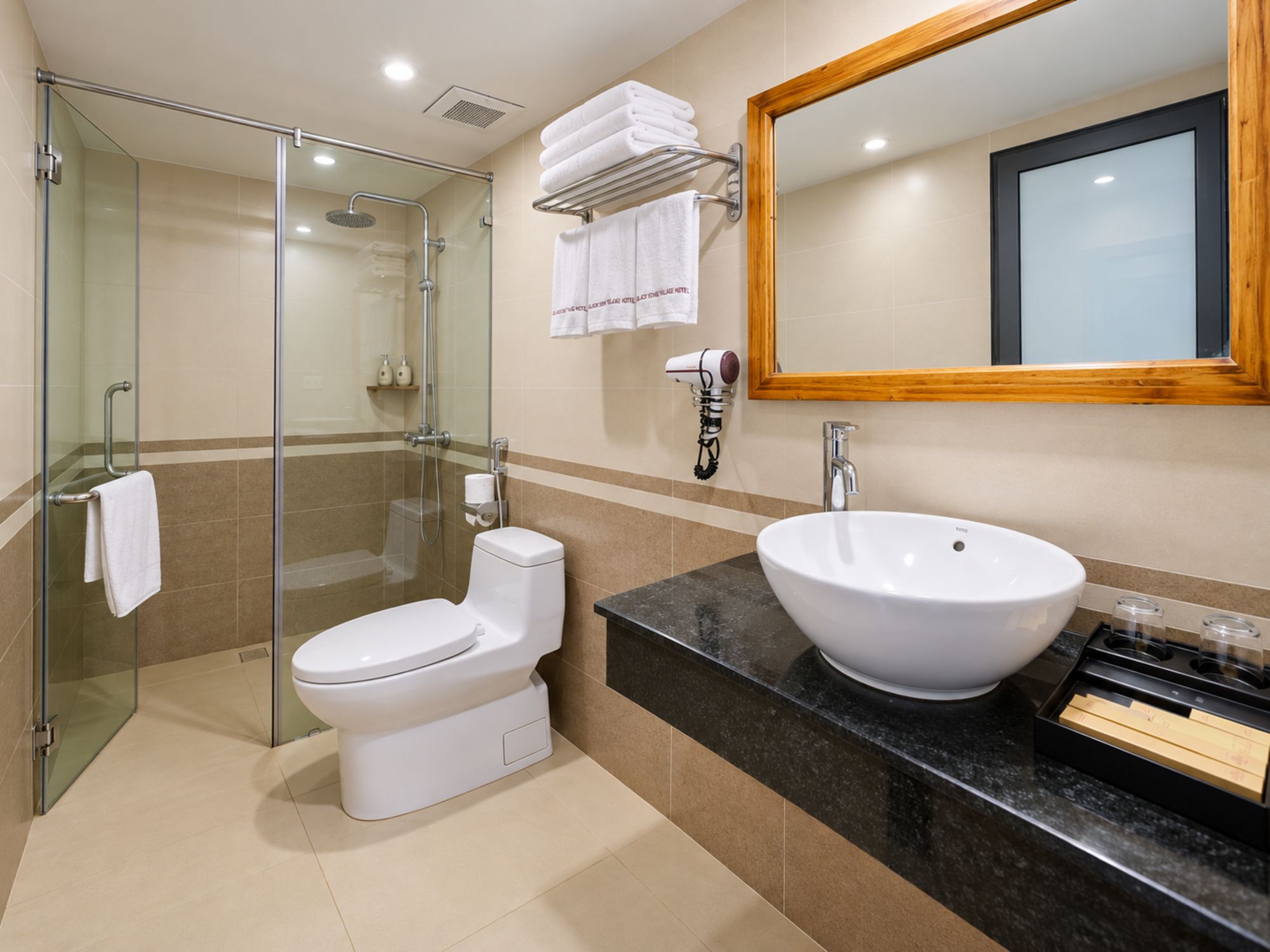 Un baño moderno con ducha de vidrio, inodoro blanco, lavabo grande y espejo con marco de madera.