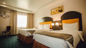 Ein Hotelzimmer mit zwei Betten, einem Sessel, einem Schreibtisch und einem fensterbepflanzten Fenster.