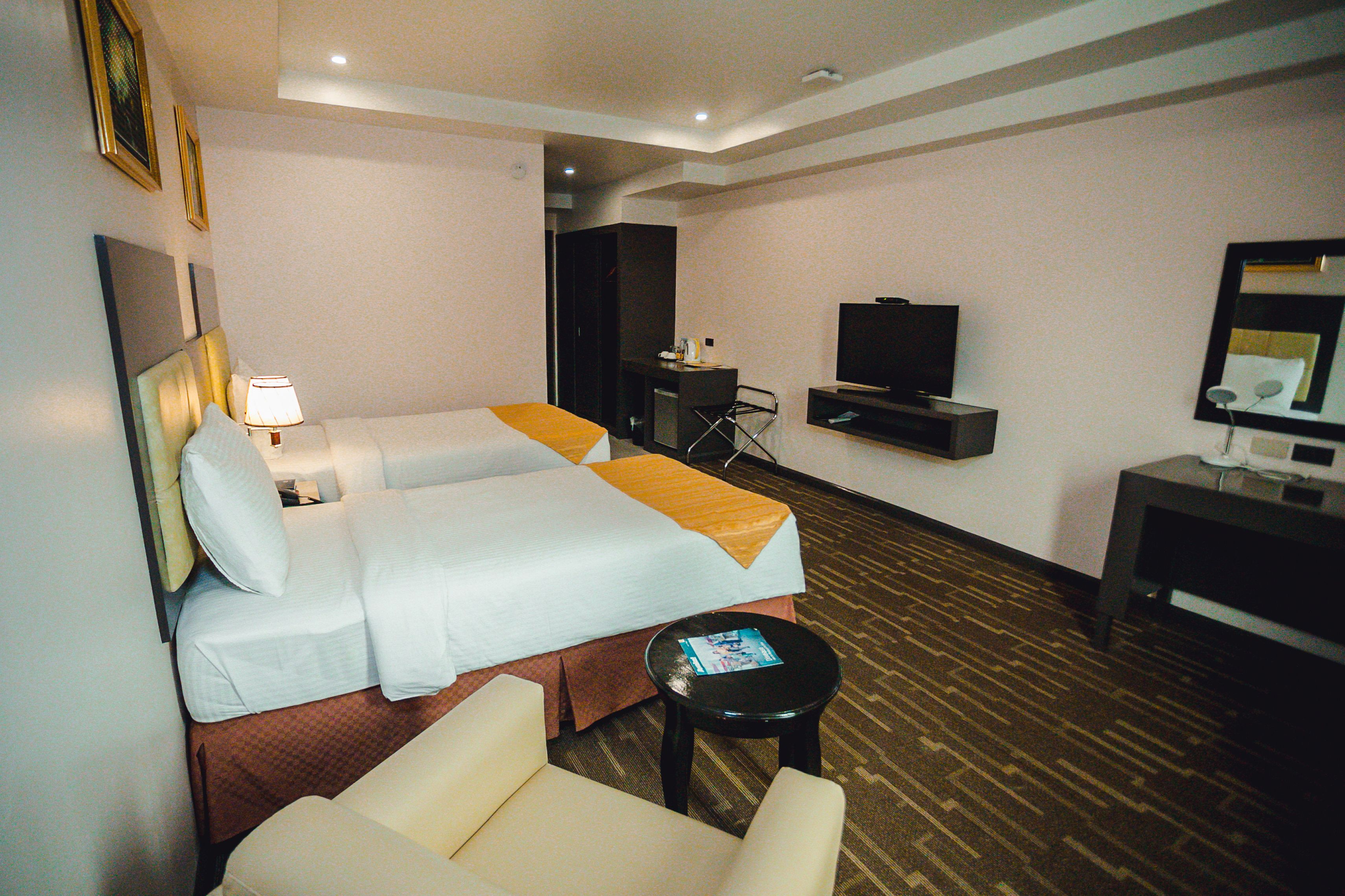 A hotel room with two beds, a desk, a television, and a chair.