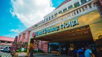 Grand Palace Hotel features a grand entrance with a large sign, balcony, and red roof.